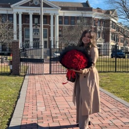 Woman holding a large bouquet of red roses in front of a school building