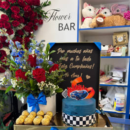 Red rose arrangement with blue flowers, chocolates, and a blue cake in a gift box