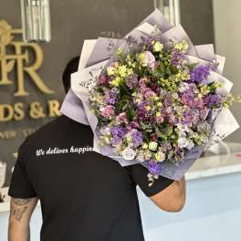 Large bouquet of purple, pink, and white flowers wrapped in lavender paper