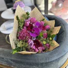 Pink and purple bouquet with roses and orchids wrapped in newspaper-style paper