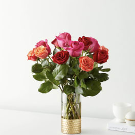 Bouquet of red, pink, and peach roses in a clear glass vase