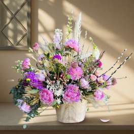 Large pink and purple floral arrangement in a light wood vase