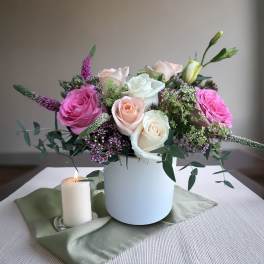 Pink and white roses in a white vase with a lit candle