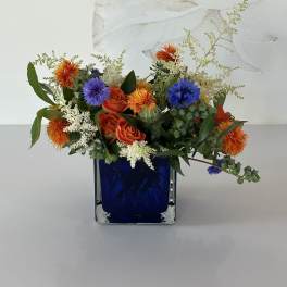 Mixed bouquet of orange and blue flowers in a cobalt glass vase