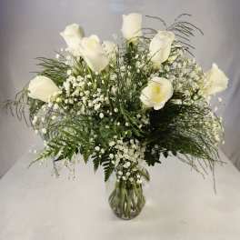 White roses arranged in a clear glass vase with airy filler flowers