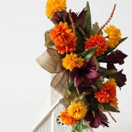 Orange and burgundy floral arrangement in a white decorative house container