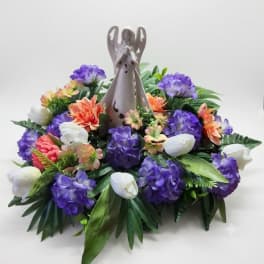Purple and white floral arrangement with orange accents around a ceramic angel figurine