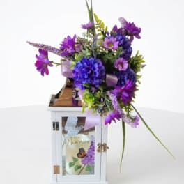 Purple floral arrangement in a white lantern with a candle inside