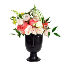 Pink and white roses arranged in a black face-shaped vase