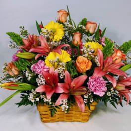 Colorful basket arrangement with pink lilies, yellow gerberas, orange roses, and pink carnations.