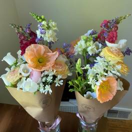 Two mixed bouquets with pastel poppies, snapdragons, and daisies in kraft wrap