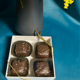 Yellow fluffy flowers in a dark vase beside a white box of four salted chocolate candies