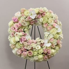 Circular floral wreath of pink and cream roses on a black stand