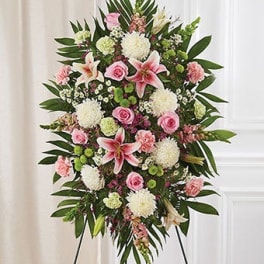 Standing floral spray with pink lilies, roses, and white blooms on an easel