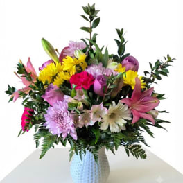 Mixed bouquet of pink, yellow, and lavender flowers in a white vase