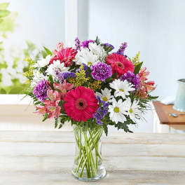 Mixed bouquet of pink, white, and purple flowers in a clear glass vase