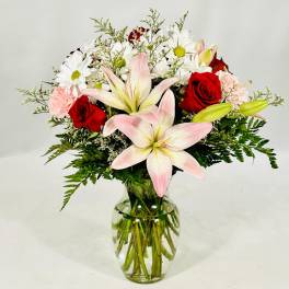 Bouquet of pink lilies, red roses, and white daisies in a glass vase