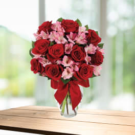 Red roses and pink alstroemeria in a clear glass vase with a red bow