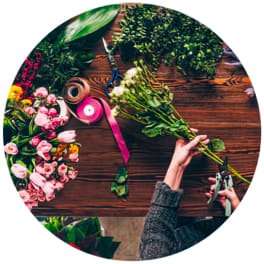 Hands trimming a bouquet of pink flowers on a wooden table