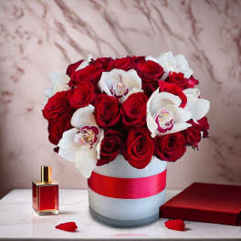 Red roses and white orchids arranged in a round vase with a red ribbon.