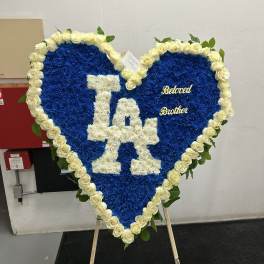 Heart-shaped blue floral tribute with white roses and "LA" lettering