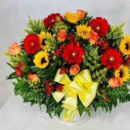 Mixed bouquet of red gerbera daisies, yellow sunflowers, and orange roses in a clear vase