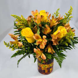 Yellow roses and orange alstroemeria in a mosaic glass vase.