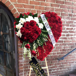 Heart-shaped standing funeral arrangement of red and white roses with memorial ribbons on an easel.