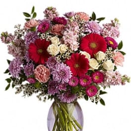 Mixed bouquet of pink, purple, and red flowers in a glass vase