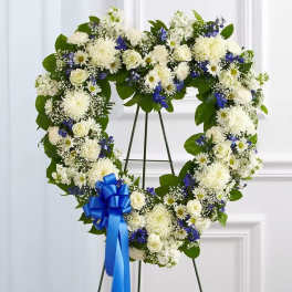 Heart-shaped floral wreath with white and blue flowers on a stand