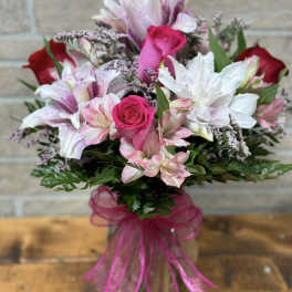 Pink and red roses with white and pink lilies in a clear glass vase with a pink bow.