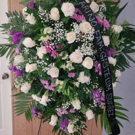Standing funeral wreath of white and purple flowers with a black memorial ribbon
