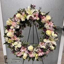 Standing wreath of pink daisies, white roses, and lilies on a green easel.