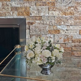 White floral arrangement in a silver urn on a glass ledge