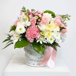 Pink and white mixed bouquet in a white basket with a pink ribbon
