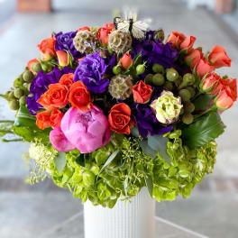 Colorful bouquet of roses and purple blooms in a white vase