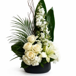 White roses, lilies, and tall white blooms in a black vase with large green leaves