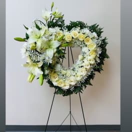 Heart-shaped white floral wreath on a stand with lilies and roses