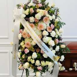 Standing funeral spray of white and blush flowers with ribbons on an easel