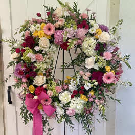 Large floral wreath on a black stand with a pink ribbon