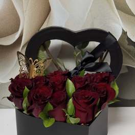 Red roses in a black heart-shaped gift box with a butterfly pick