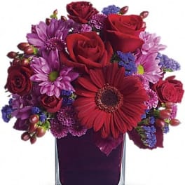Red roses and purple flowers arranged in a square glass vase