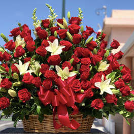 Basket arrangement of red roses and white lilies with a red ribbon