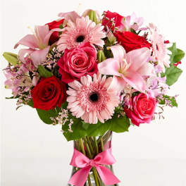 Bouquet of pink lilies, red roses, and pink gerbera daisies in a glass vase