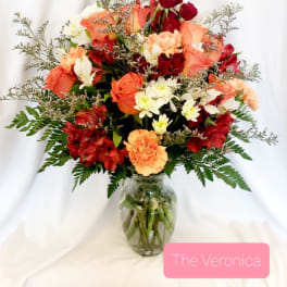 Mixed bouquet of red, peach, and white flowers in a glass vase
