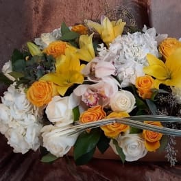 Yellow lilies and orange roses arranged with white blooms in a low container