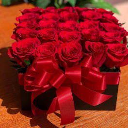Red roses arranged in a black box with a red ribbon bow