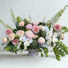 Low floral arrangement with pink blooms, white orchids, and green accents in a gray vase