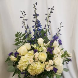 Tall bouquet of white roses, hydrangeas, and blue delphinium in a glass vase