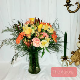 Mixed bouquet of orange, yellow, and pink flowers in a glass vase